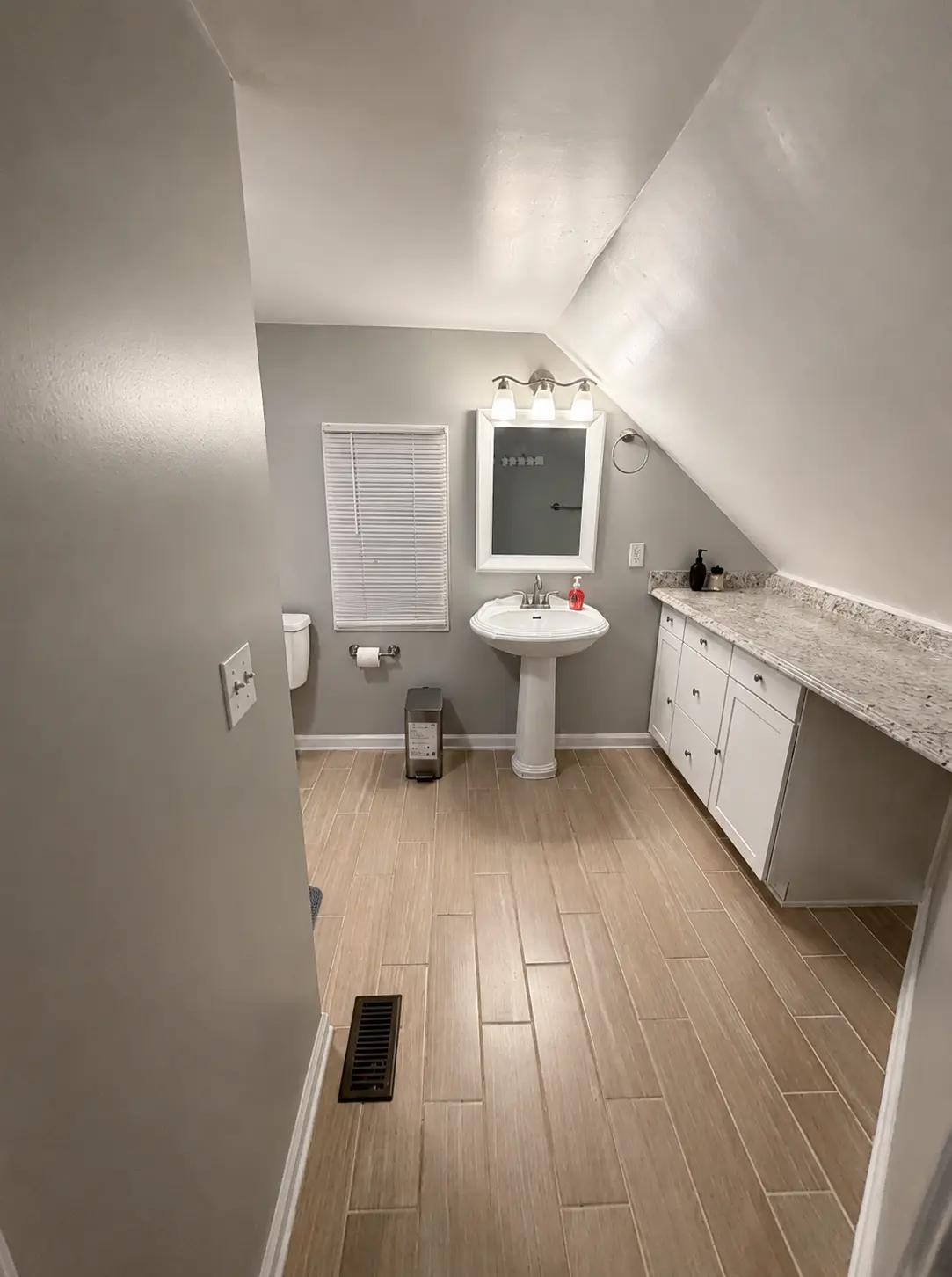 Upstairs bathroom with pedestal sink, mirror, vanity light and a granite-topped counter along the sloped wall