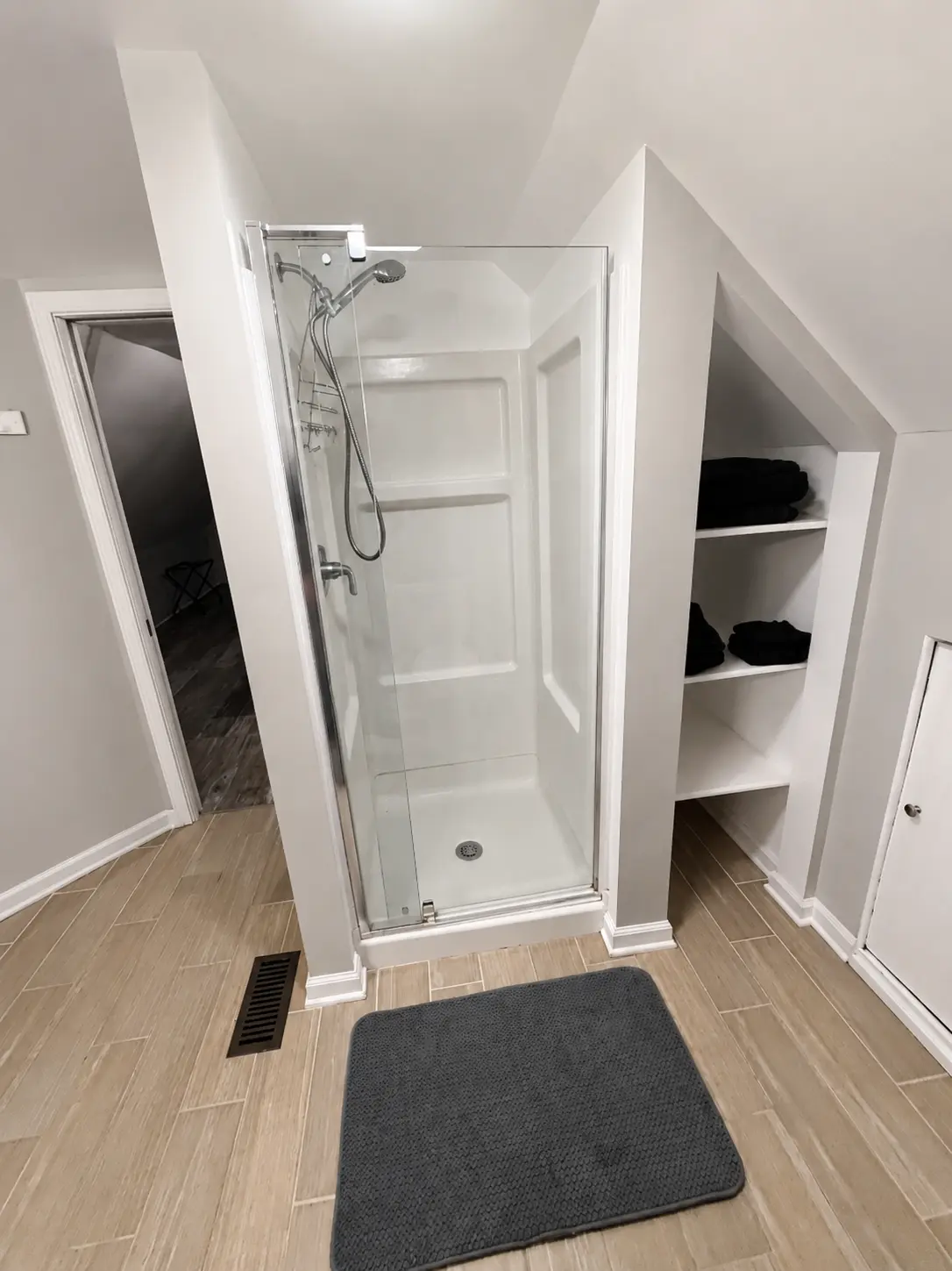 Upstairs bathroom shower stall with glass door and built-in shelving holding folded towels