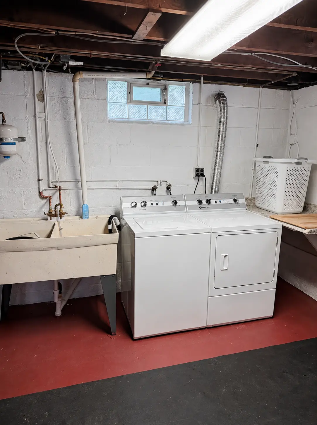 Basement laundry area with a washer and dryer, utility sink and glass block window