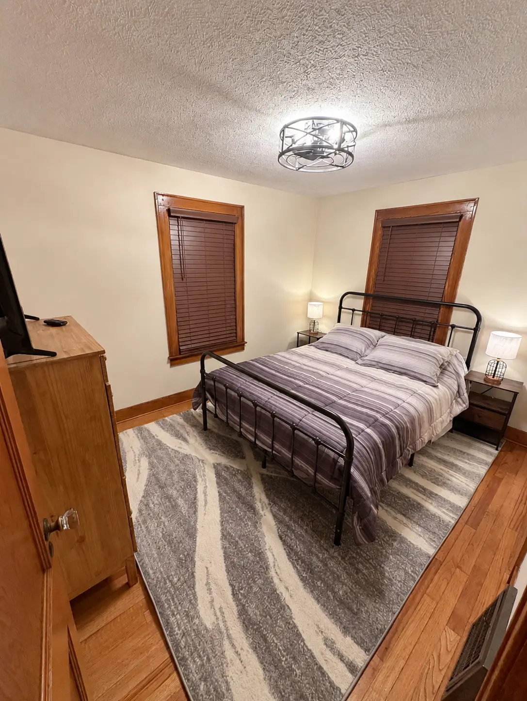 Main floor bedroom with a queen bed, striped bedding, wood dresser and television