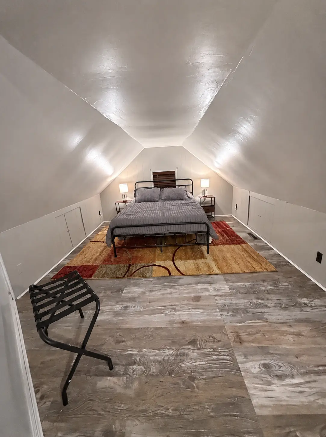 Long view of the upstairs bedroom under sloped ceilings with a queen bed and luggage rack