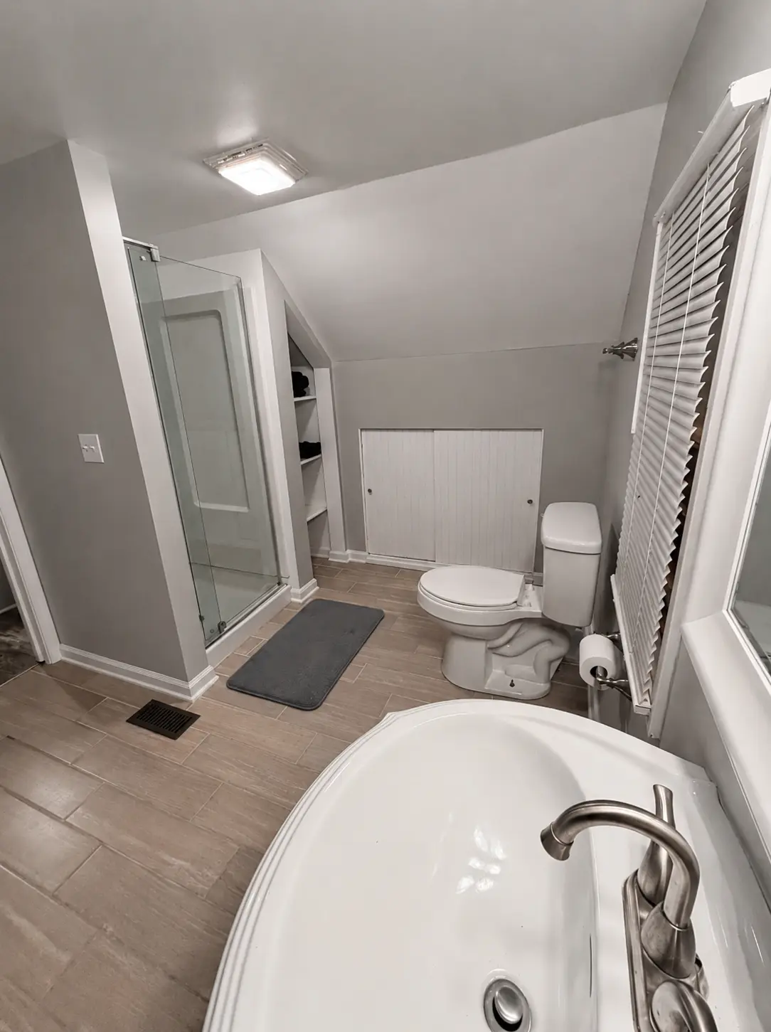 Second view of the upstairs bathroom showing the shower, toilet, window blinds and tile flooring